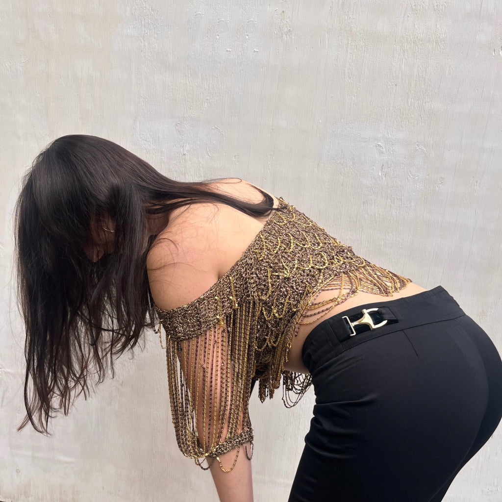 Person wearing a gold fringe top and black pants against a plain background